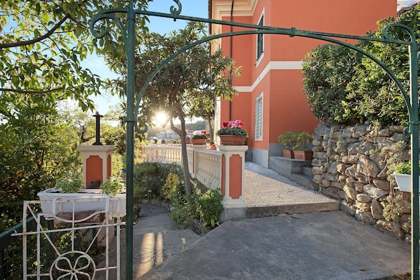 A courtyard with a stone wall, a metal gate, and a building with a red facade.