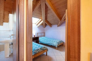 A bedroom with two single beds, a wooden ceiling, a skylight, and a bathroom with a sink and toilet.