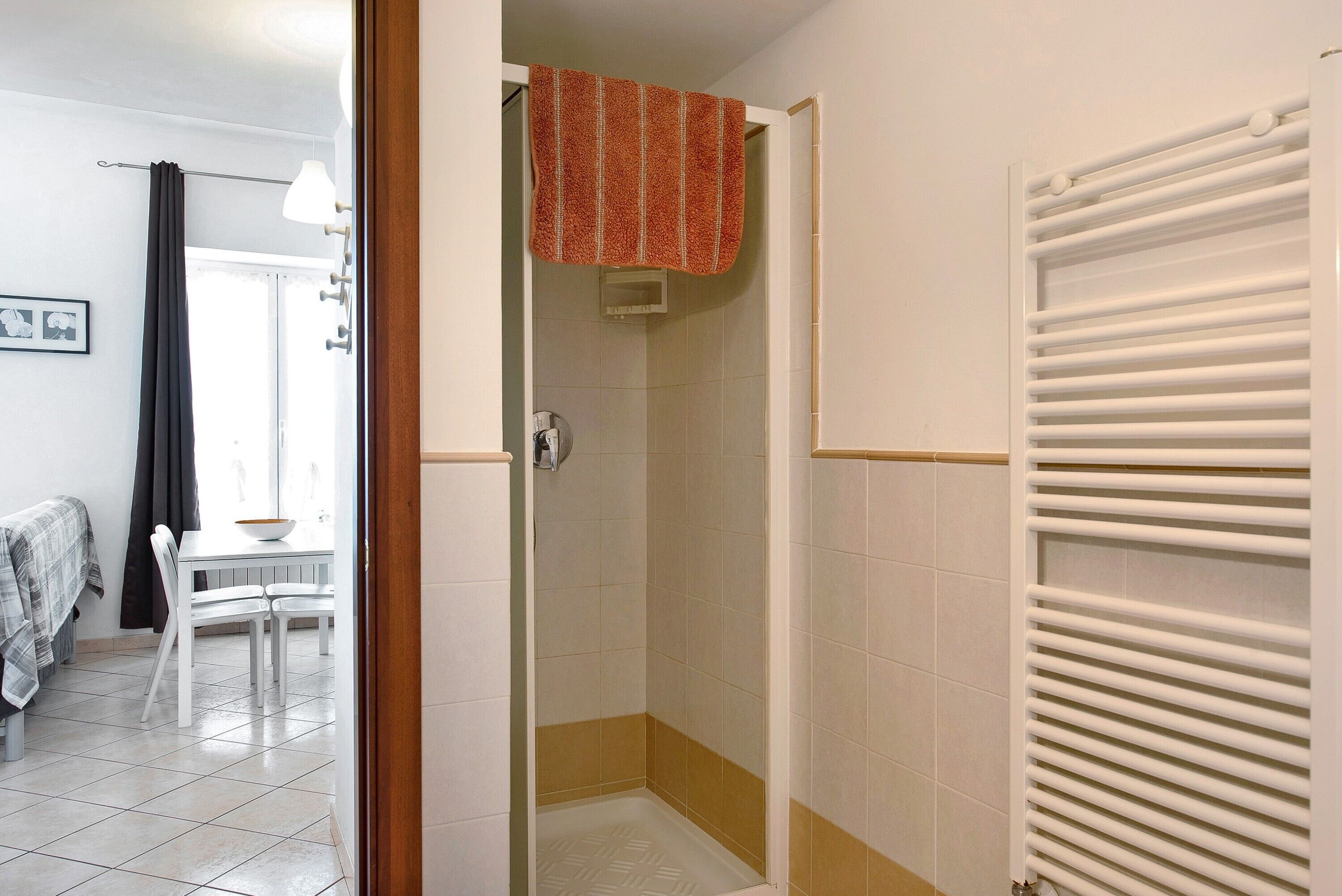 Une salle de bain avec une douche, une serviette accrochée au mur, un radiateur et un sol carrelé.