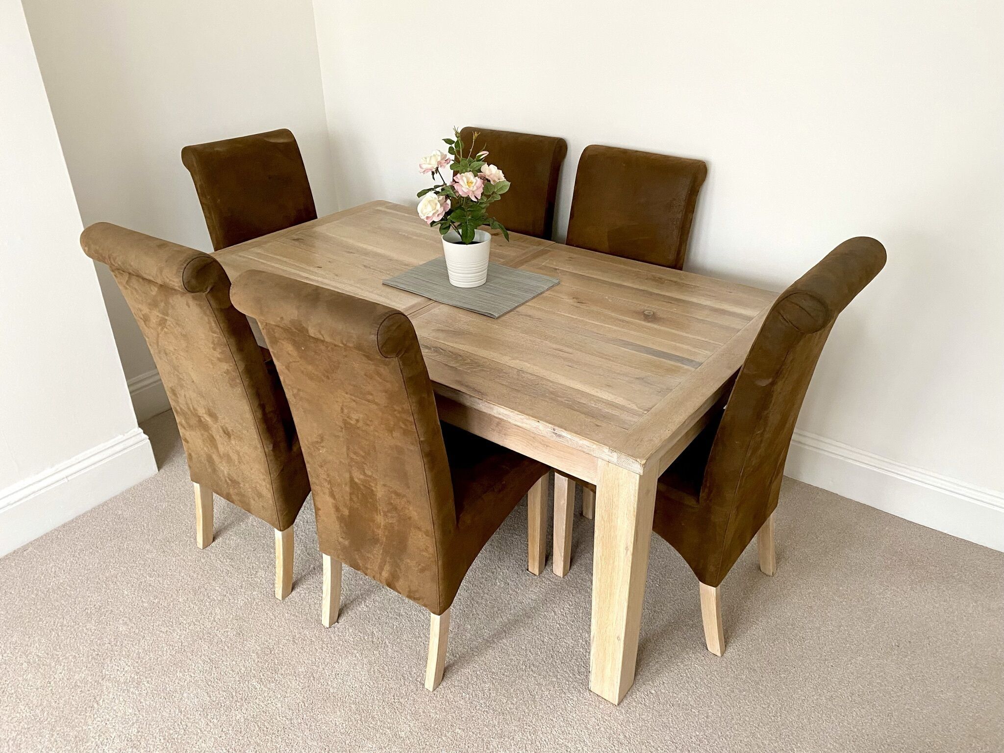 A wooden dining table with six brown upholstered chairs, a white vase with flowers, and a gray placemat.
