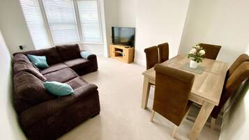 A living room with a brown sofa, a wooden dining table, and a TV stand.