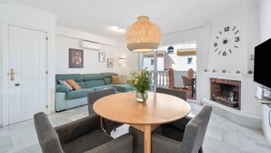 A living room with a round wooden table, grey sofas, a hanging light fixture, a wall clock, and a fireplace. - Holiday home "Balcon de Benalmadena Ocean Views" with Pool, Terrace & Wi-Fi [only guests over 25] (Benalmádena)