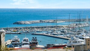 A marina with boats docked, a rocky breakwater, and a clear blue sky.