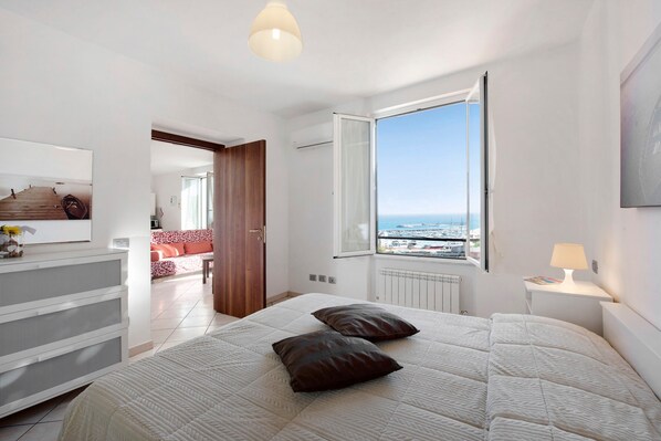A bedroom with a large bed, a view of the sea, a window, and a white dresser.