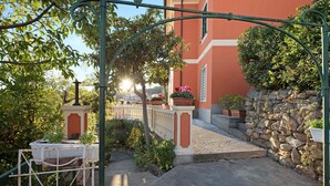 A courtyard with a stone wall, a metal gate, and a building with a red facade.