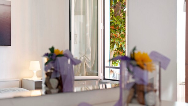 A bedroom with a bed, a nightstand, a lamp, and a window with a view of greenery.