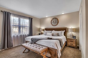 Une chambre à coucher avec un grand lit, des tables de chevet, un banc et un élément décoratif mural.