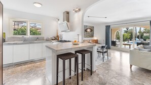 Una cocina moderna con una isla central, taburetes de bar y un comedor con sofá y sillas.