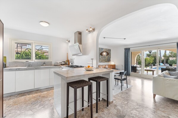 A modern kitchen with a central island, bar stools, and a dining area with a sofa and chairs.