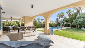 Un espacio al aire libre techado con piscina, zona de comedor y vistas a la vegetación circundante.