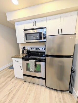 A kitchen with stainless steel appliances, including a microwave, oven, and refrigerator, with white cabinetry and a granite countertop.