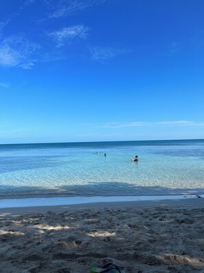 A beach with clear water, a sandy shore, and a few people swimming.
