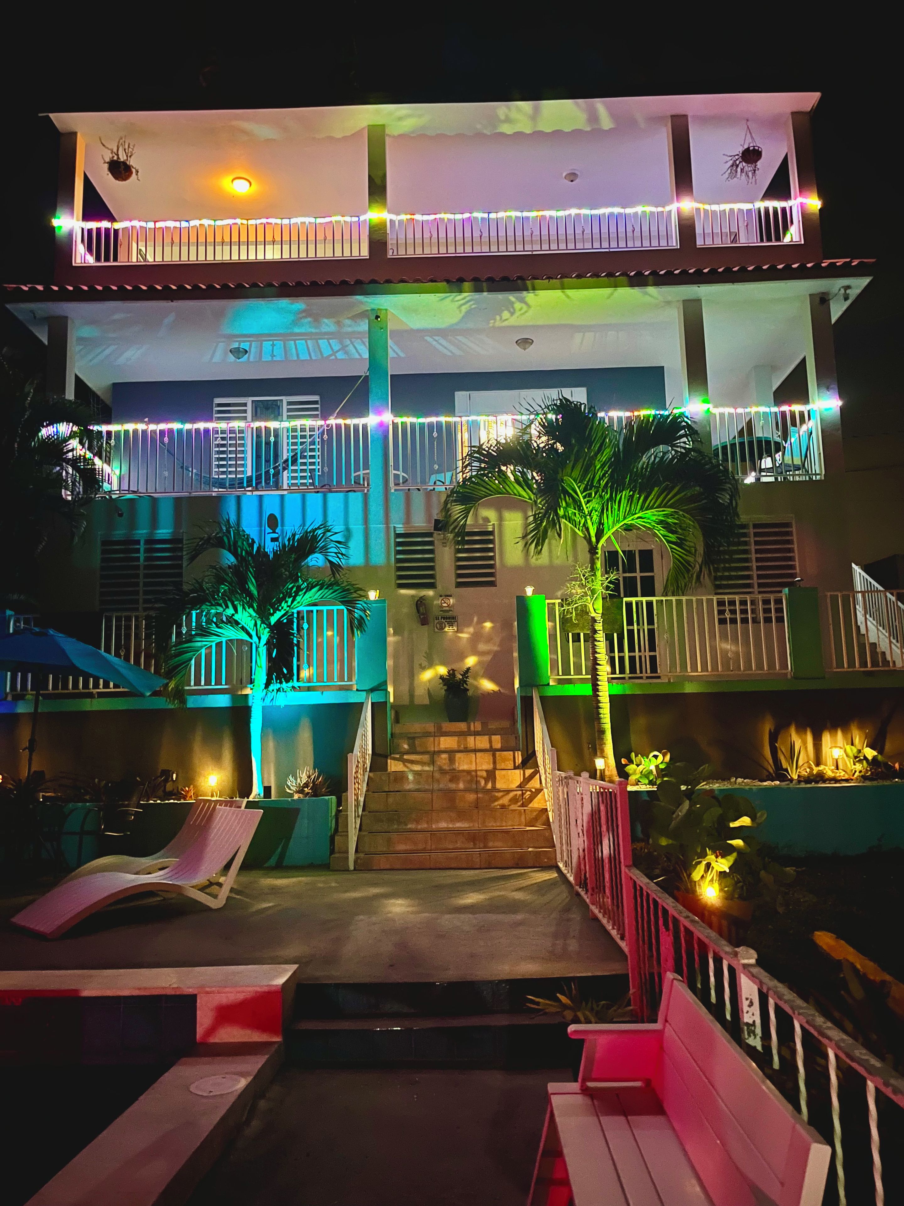 A two-story building with a balcony on the upper level, a staircase leading to the entrance, and outdoor seating areas.