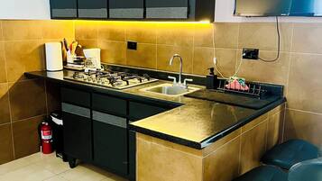 Cocina con isla central, armarios negros, salpicadero azulejado, estufa a gas, un lavamanos y dos taburetes de bar.