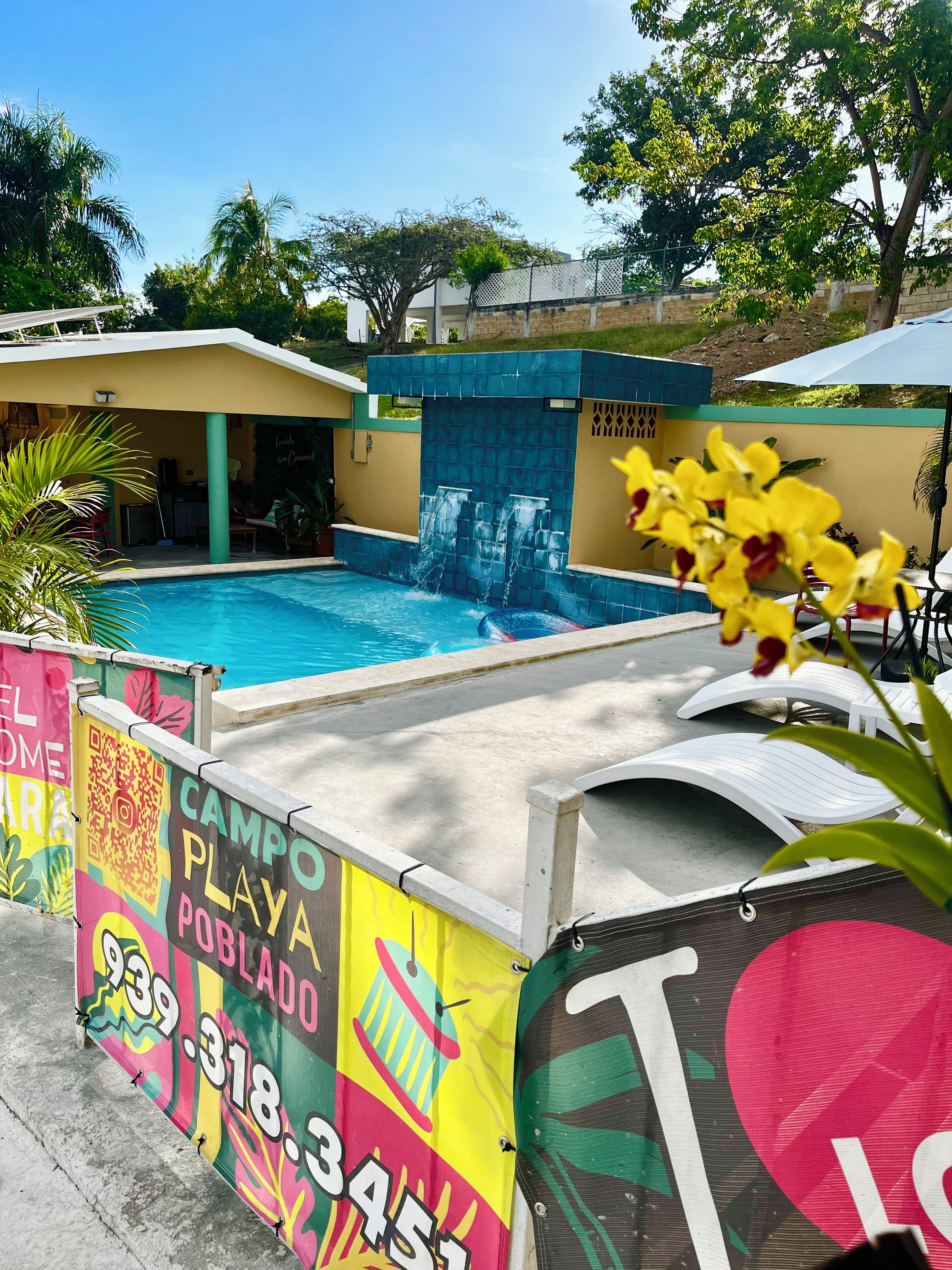 Piscina con caída de agua, rodeada por una valla colorida con un código QR e información de contacto.