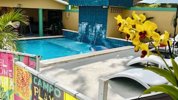 Piscina con caída de agua, rodeada por una valla colorida con un código QR e información de contacto.