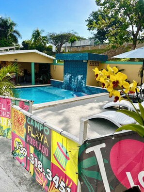 Una piscina amb cascada, envoltada per una tanca colorida amb un codi QR i informació de contacte.