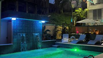 A swimming pool with a waterfall feature, surrounded by lounge chairs and a covered seating area.