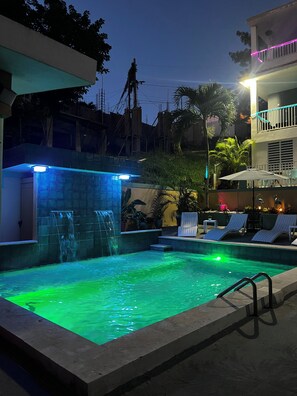 A swimming pool with a waterfall feature, surrounded by lounge chairs and a covered seating area.