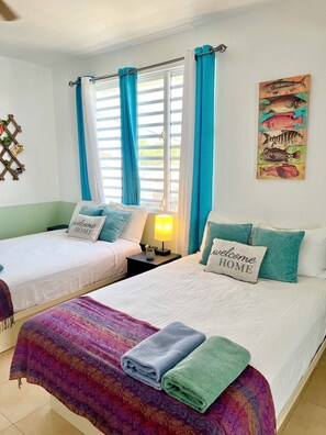 Una habitació d'hotel amb dos llits, una finestra amb cortines, una obra d'art penjada a la paret i una taula de nit amb una làmpada.