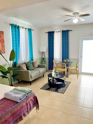 A living room with a sofa, a coffee table, a dining table with chairs, a ceiling fan, and a window with curtains. - Estudio with Bay views mins to Poblado de Boqueron & Heated Pool (3A) (Boquerón)