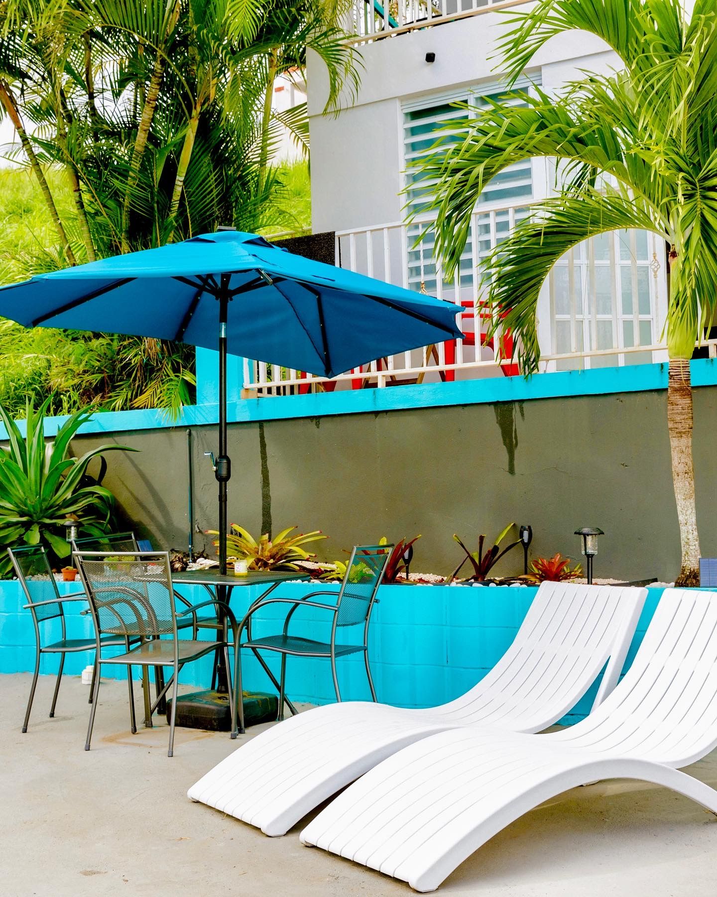 Zona junto a la piscina con sillas de descanso, una mesa y una sombrilla.