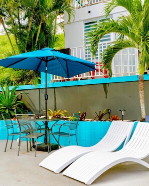 A poolside area with lounge chairs, a table, and an umbrella.