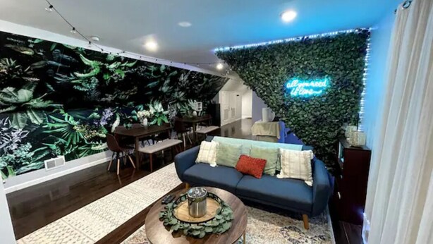 Ein modernes Wohnzimmer mit einem blauen Sofa, einem Couchtisch und einer Wandmalerei von tropischen Pflanzen.