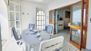 A dining area with a round table, chairs, and a view of the kitchen through an open door. - Casa Giasone: A characteristic and welcoming apartment that is part of a villa built sheer above the sea and with direct access to the sea, with Free WI-FI. (Praiano)
