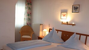 A double bed with two pillows, a nightstand with a lamp, a wicker chair, and a framed picture on the wall. - Wohnung Nr. 5 Sonnenrose 56 qm mit einem Schlafzimmer, zwei Bäder und Südbalkon (Bad Reichenhall)