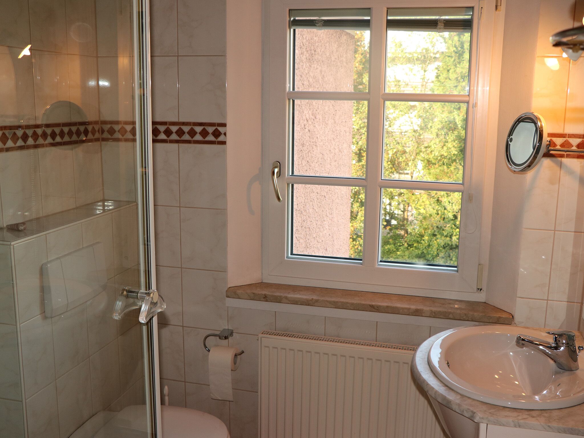 A bathroom with a window, a toilet, a sink, and a shower.