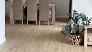 Un comedor con una mesa de madera y cuatro sillas, una lámpara colgante tejida y una planta en maceta.