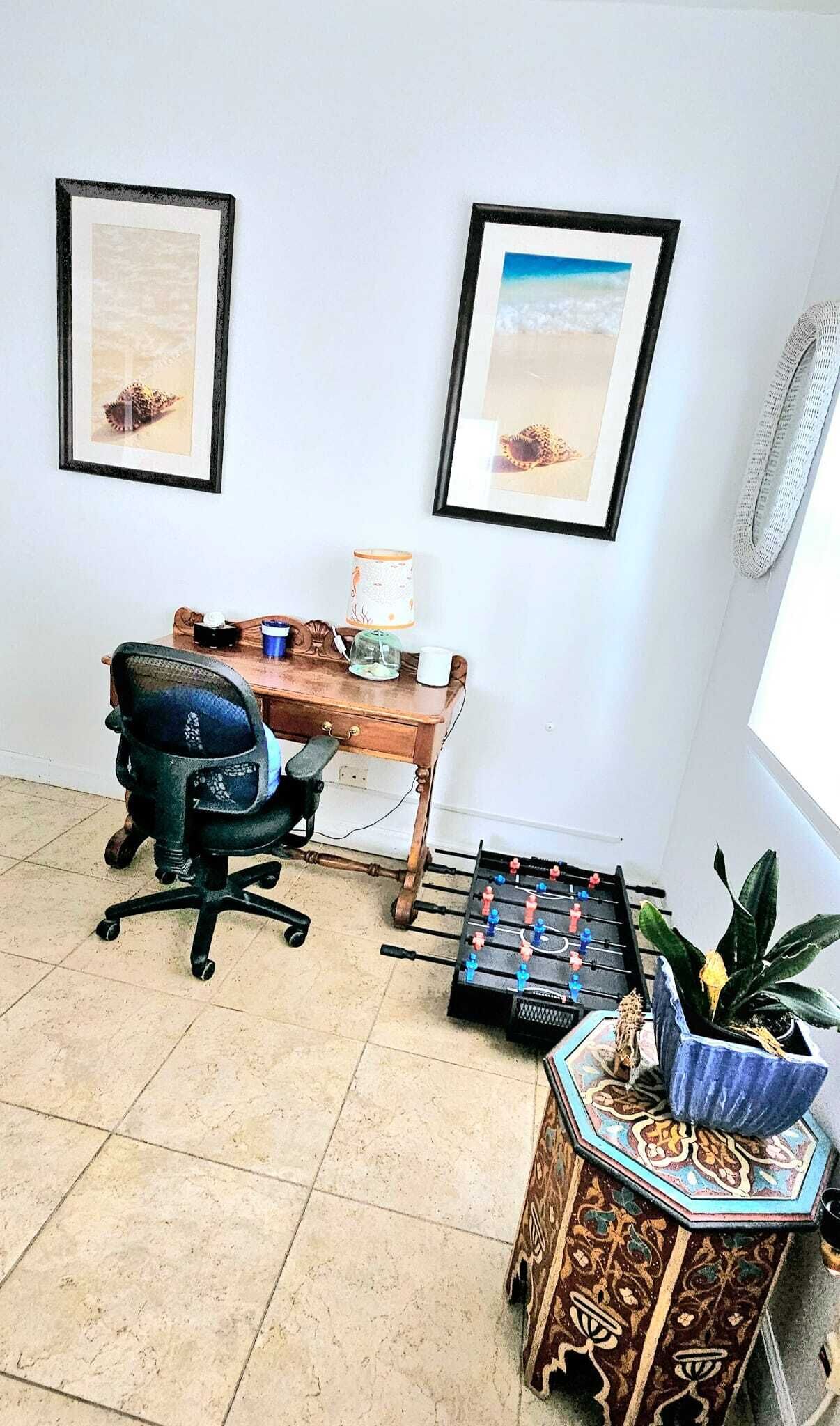 Una habitación con escritorio, dos cuadros, una silla, una mesa de fútbol y una planta.