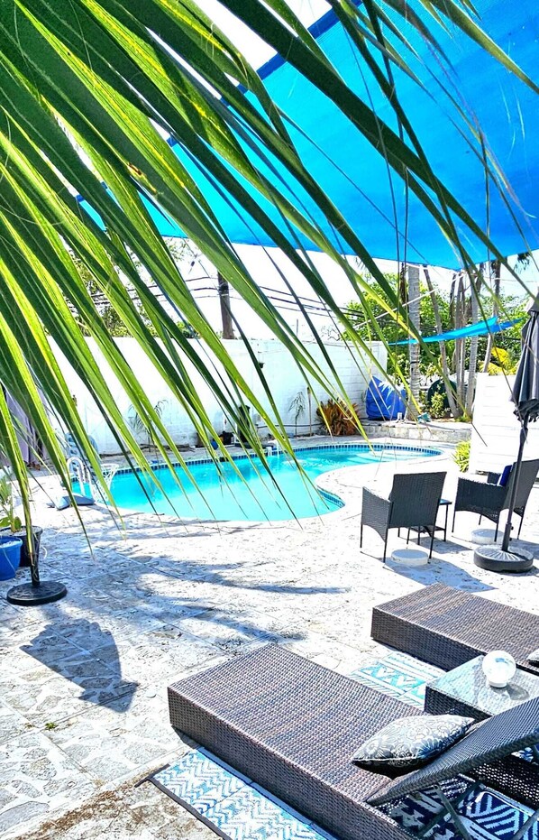 Un espace aménagé au bord de la piscine, avec des chaises longues, une piscine et un parasol bleu pour offrir de l’ombre.