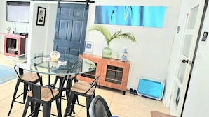 A dining area with a glass table and black metal chairs, a blue door, a wall-mounted painting, and a small cabinet with decorative items.