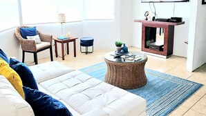 A living room with a white sofa, a wicker coffee table, a flat-screen TV, and a large window.