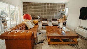 A modern living room with a leather sofa, wooden coffee table, and a large TV. - Gorgeous 5 bedroom beach house. Dog/Kid Friendly. (Marcoola)