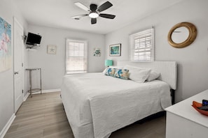A bedroom with a bed, a ceiling fan, a TV, a window, and a wall-mounted mirror. - Channel home 3 blocks from beach-fish, crab-2 porches and ping-pong-perfect family getaway (North Myrtle Beach)