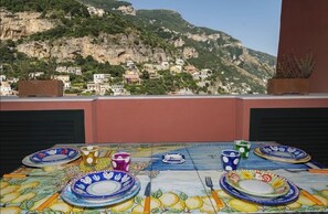 Ein Tisch mit bunten Tellern und Tassen, mit Blick auf ein dörfliches Bergpanorama.