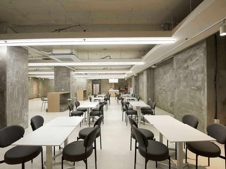 Una sala de conferències amb taules i cadires blanques, un escenari i una taula llarga al centre.