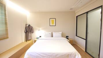 A modern bedroom with a large bed, bedside tables, a robe hanging, and a sliding glass door.