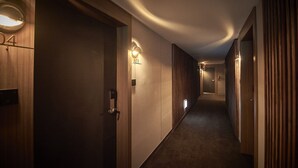 A hallway with wooden doors, numbered room signs, and wall-mounted lighting. - Bonathree Hotel (Busan)