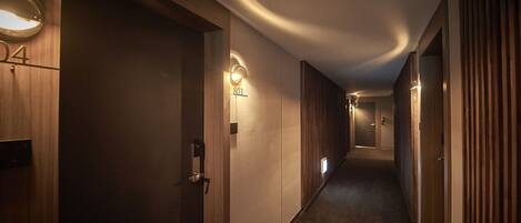 Un pasillo con puertas de madera, letreros de habitaciones numeradas e iluminación empotrada.