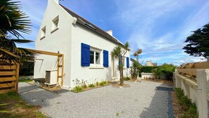 A white building with blue shutters, a gravel driveway, and surrounding greenery. - Le Petit Pingouin, sleeps 6, sea and beach 300 metres away (Cléder)