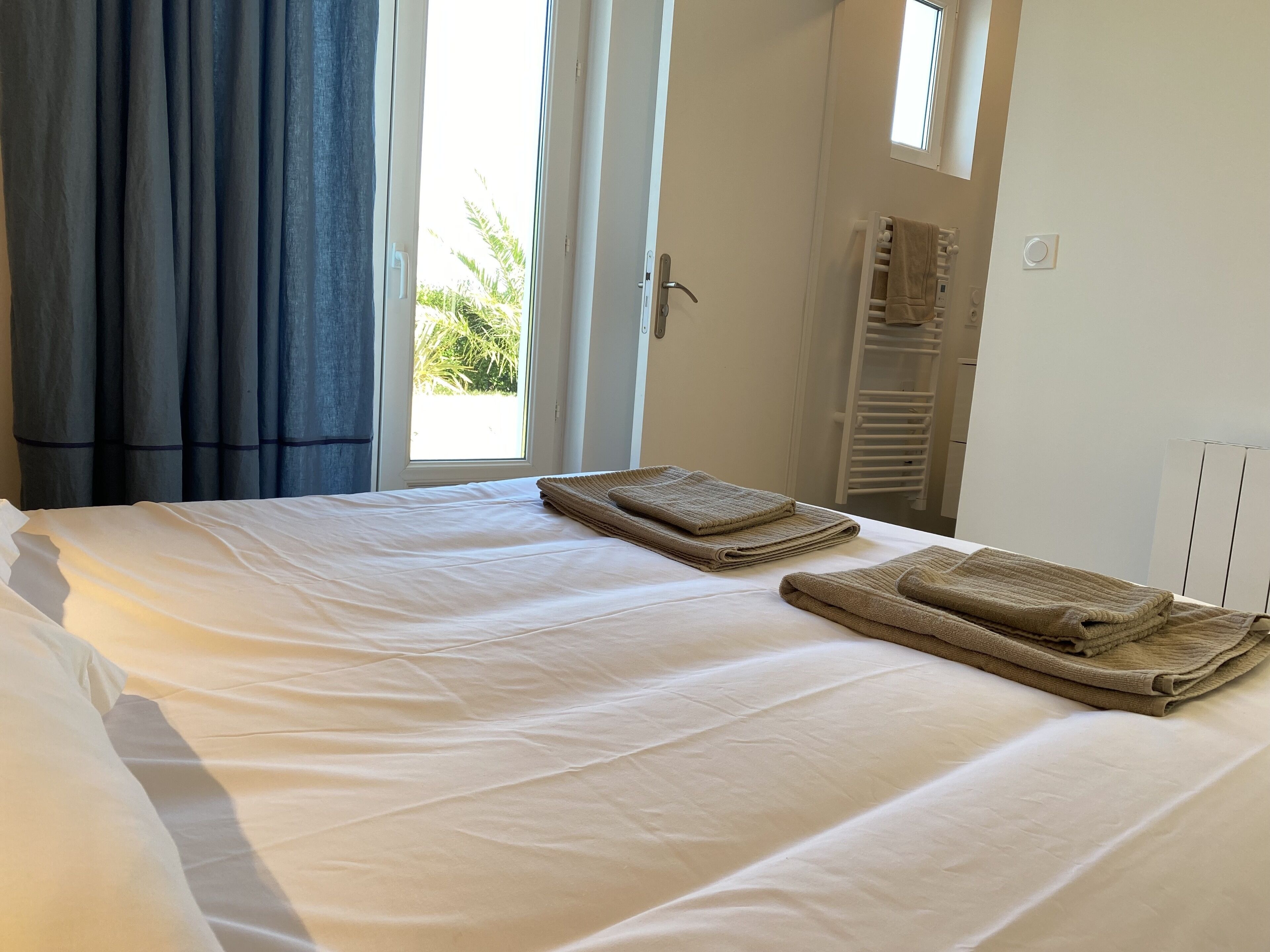 A neatly made bed with white linens and two folded towels.