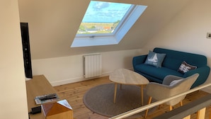 A modern loft bedroom with a skylight, a blue sofa, and a wooden desk. - Le Petit Pingouin, sleeps 6, sea and beach 300 metres away (Cléder)