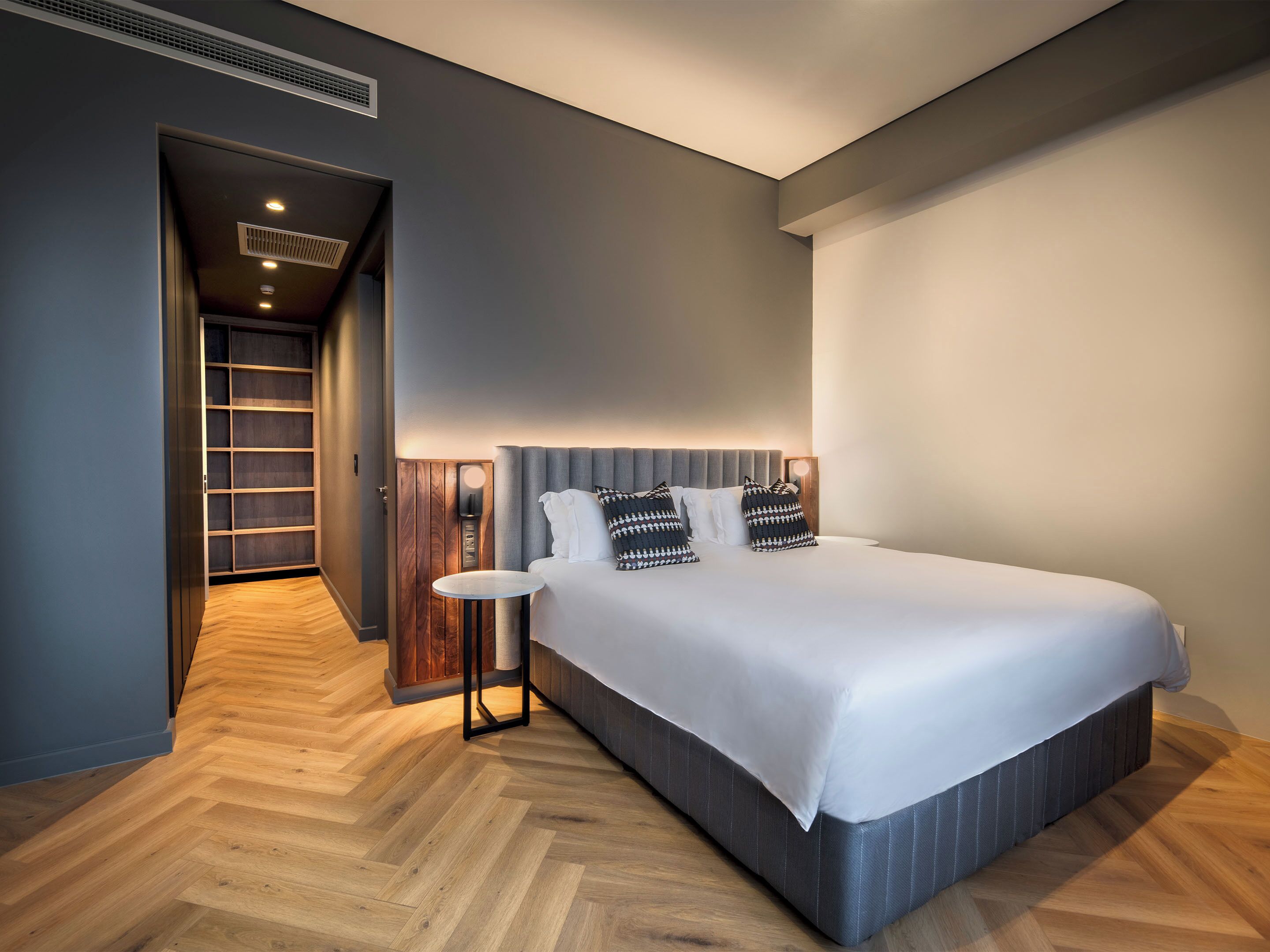 A modern hotel room with a large bed, a bedside table, a wardrobe, and a walk-in closet.