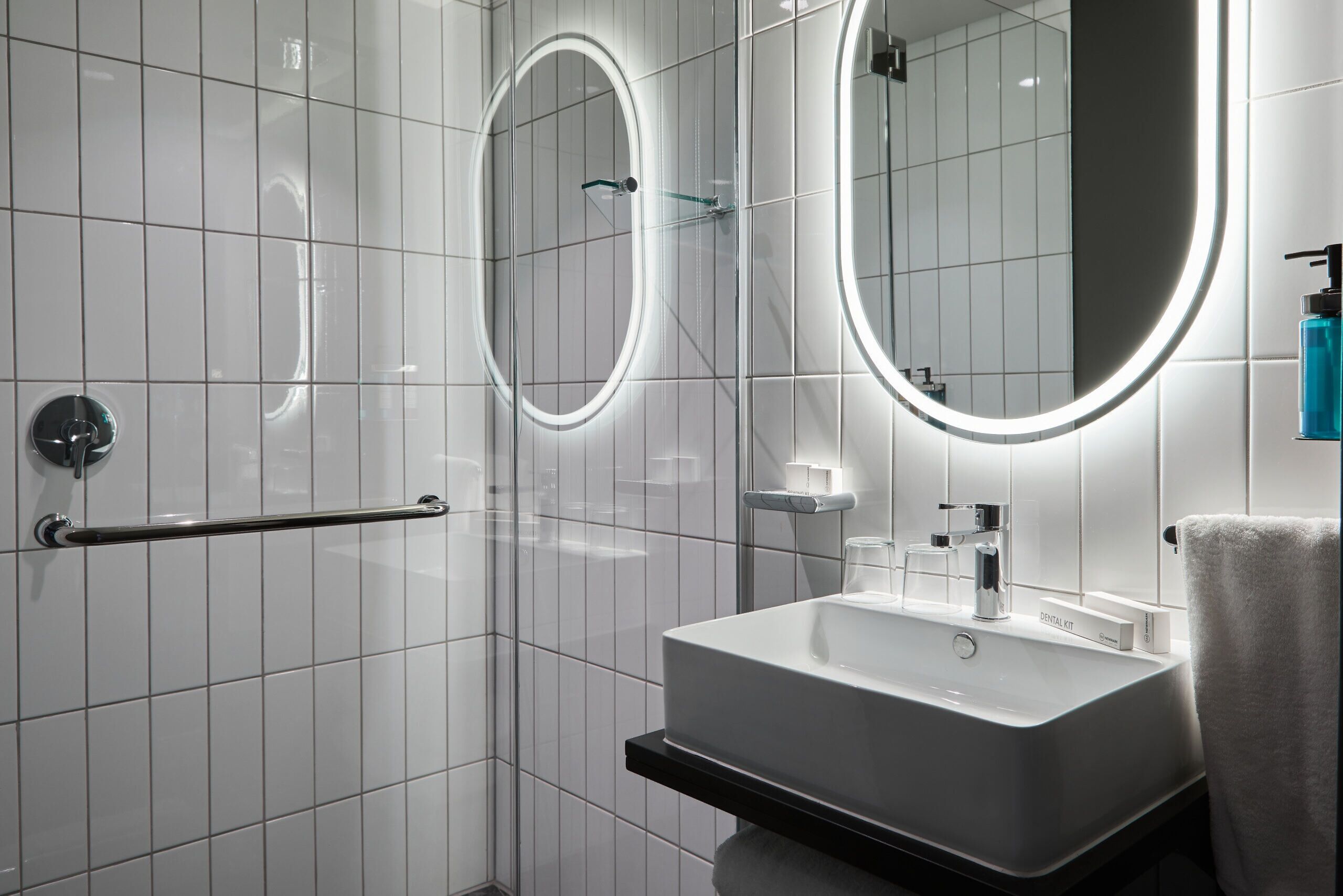 A modern bathroom with a white sink, two mirrors, and a glass shower enclosure.