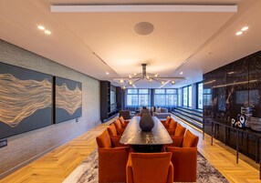 A modern dining area with a long table, orange chairs, and a unique chandelier.