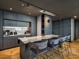 A modern kitchen with a marble countertop, built-in appliances, and a bar area with velvet barstools.